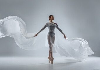 Ballerina in dark ballet leotard dancing on ballet pointe shoes in white studio 