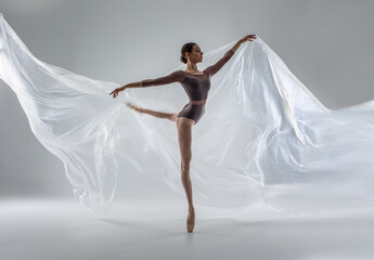 Ballerina in dark ballet leotard dancing on ballet pointe shoes in white studio  - obrazy, fototapety, plakaty