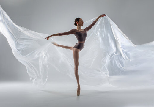 Fototapeta Ballerina in dark ballet leotard dancing on ballet pointe shoes in white studio 