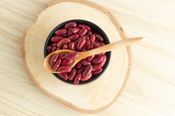 red kidney beans in a black bowl and spoon on wooden background, top view, flat lay, top-down, selective focus.
