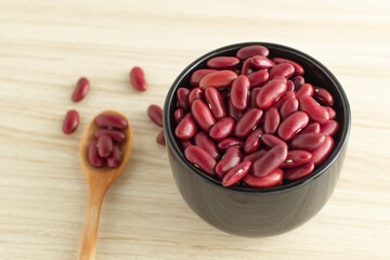 red kidney beans in a black bowl and spoon on wooden background, front view, selective focus.