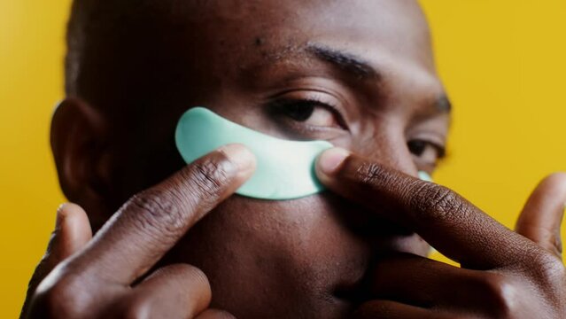 A man corrects moisturizing patches under his eyes,close-up, studio background