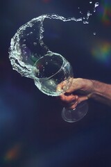 Una mano derramando el agua de una copa de cristal, cuyo movimiento queda congelado en el aire.