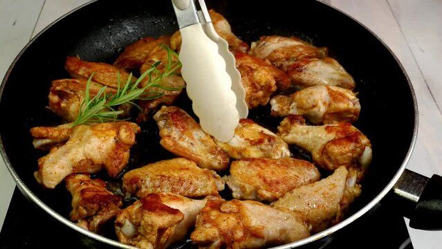 Many sprinkled with spices sliced chicken wings, preparation and turning in hot frying pan.
