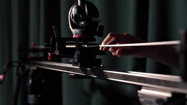 A male cameraman of a TV channel uses a slider to film a video of a talk show, news, movie or concert in a TV studio. The videographer shoots video content under professional studio lighting.