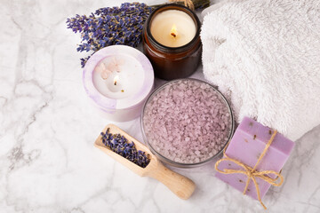 Obraz na płótnie Canvas Lavender spa.Sea salt,lavender flowers,aroma candle,body cream and handmade soap.Natural herbal cosmetics with lavender flowers on marble background.Relax concept.Beauty treatments.Copy space.