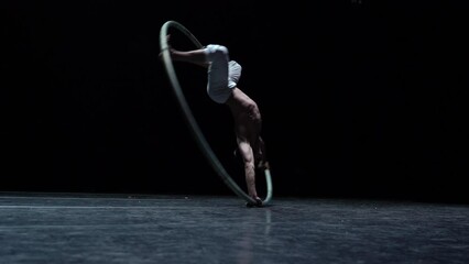 Muscular circus artist perform Cyr Wheel on a black background. Concept of willpower, motivation and healthy lifestyle