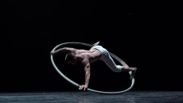 Muscular circus artist perform Cyr Wheel on a black background. Concept of willpower, motivation and healthy lifestyle