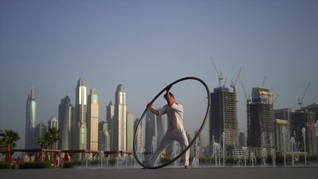 Cyr Wheel artist wearing white Arabic clothing cloth on Dubai cityscape background during sunset