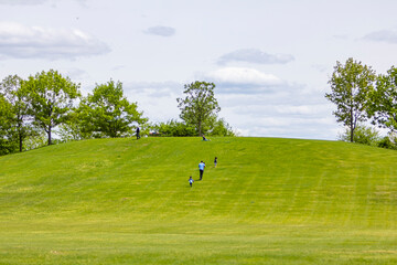 Fototapeta na wymiar A family running up a green hill during a sunny summer day with green grass on the ground and blue skies above them.