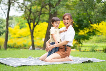 Asian young mother sit on carpet and hug her little boy in garden also look at camera with happiness during morning time.