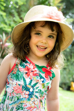 Retrato de uma criança, menina, sorrindo, feliz, com traje colorido de verão e chapéu.