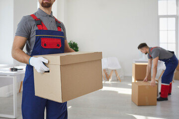 Team of male movers in uniform carry cardboard boxes with personal belongings for client during...