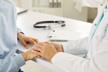 Doctor sitting at white desk with stethoscope and holding patient's hand. Female physician...