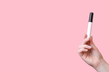 Woman holding mascara for eyelashes on pink background, closeup