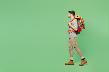 Fototapeta na wymiar Full body side view young mountaineer traveler white man carry backpack stuff mat walk isolated on plain green background. Tourist leads active healthy lifestyle. Hiking trek rest travel trip concept.