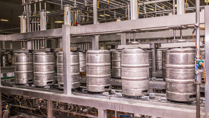 Brewery, bottling beer on aluminum kegs on conveyor lines. Industrial work, automated modern food and beverage production.