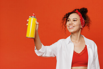 Young smiling happy fun cool woman of African American ethnicity 20s wears white shirt top hold paint spray bottle make graffiti isolated on plain orange background studio. People lifestyle concept