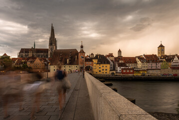 Steinerne Brücke in Regensburg im Sommer vor Gewitter mit Menschen in Bewegung