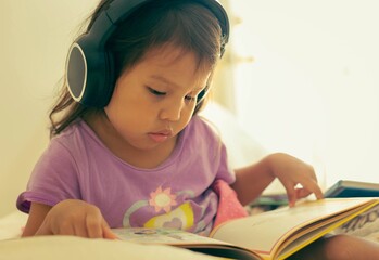 A little kid reading a book and listening to a audio. Kids learning at home.