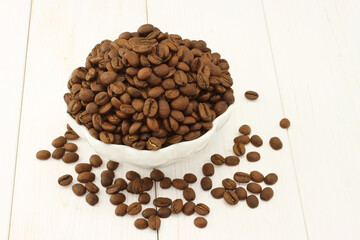 Roasted coffee beans in bowl on white wooden background
