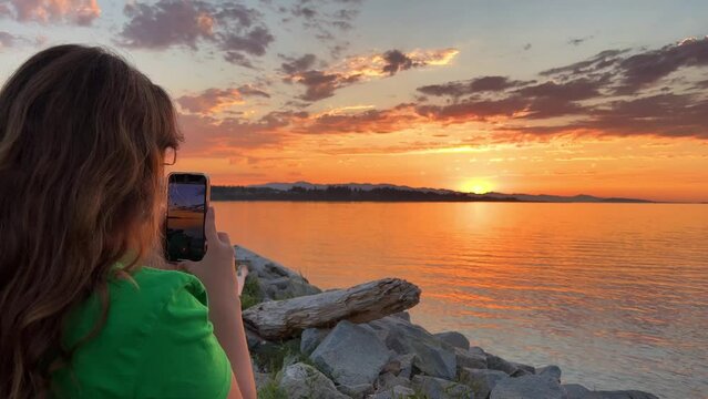 Girl texts and scrolls using phone social media applications at sunset sky seaside windy background closeup slow motion. Technologies development danger of screen addiction vs enjoying nature concept.