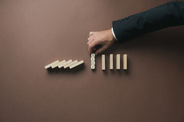 Businessman stacking wooden cubes with a Stop sign on them in the middle of collapsing dominos