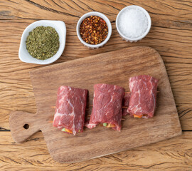 Rolled beef or roulade, vegetable and bacon stuffed meat over wooden table with seasonings