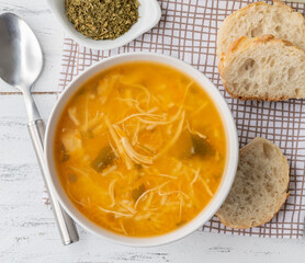 Chicken soup in a bowl with bread slices and seasoning over wooden table