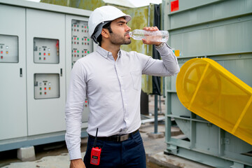 Engineer man or technician worker drink water from bottle and stand in front of electrical control...