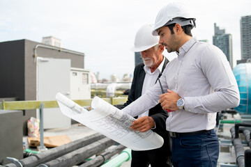 Close up shot young and senior engineer man work together using building plan or drawing in...