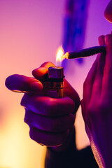 hand of a young woman lighting a joint or marijuana cigarette with a candle, psychedelic lights....