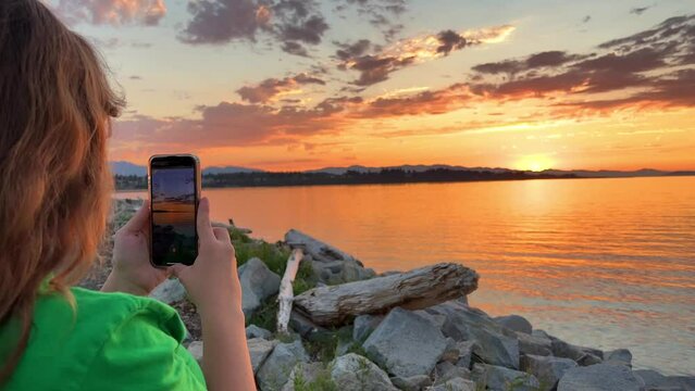 Medium shot of woman tourist on beach island taking photograph of sunset with smartphone on holiday skyline view. High quality 4k footage