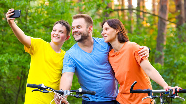 happy family takes a selfie while walking through the forest on bicycles. sports family in the forest ride bikes and take a joyful selfie. mom daddy son smile while taking a selfie