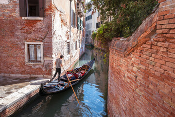 Fototapeta na wymiar Venetian young gondolier with tourists in gondola on canal waters of Venice Italy