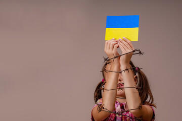 Young girl with hands in barbed wire holding flag of Ukraine as symbol of the struggle for freedom...
