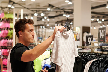 A young hispanic man looking a t-shirt in the store