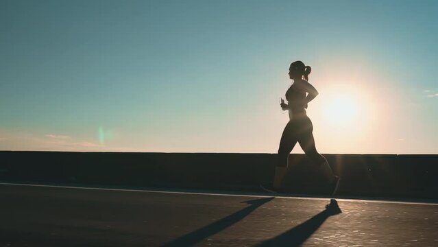The girl runs along the road at sunset, side view.