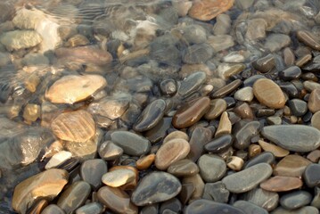A pure transparent sea wave rolls over the rocky pebble shore, the concept of rest and travel, tranquility, relaxation and reflection on a warm summer day, close-up.