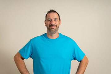 Obraz premium Cheerful bearded man in blue t-shirt posing isolated on blue background, studio portrait. People lifestyle concept. Mock up copy space. Standing with arms akimbo on waist blinking