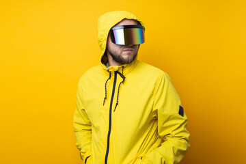 Young man in virtual reality glasses in a yellow jacket looks away on a yellow background