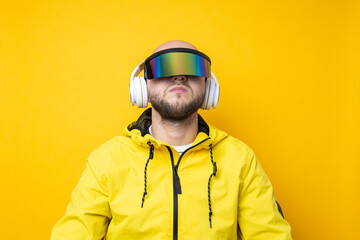 Young man in cyberpunk glasses in a yellow jacket with headphones on a yellow background