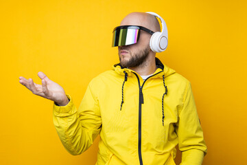 Young man in cyberpunk glasses with headphones holding an invisible object on a yellow background