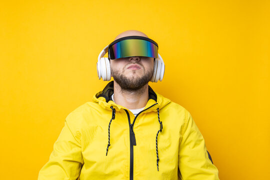 Young man in cyberpunk glasses in a yellow jacket with headphones on a yellow background