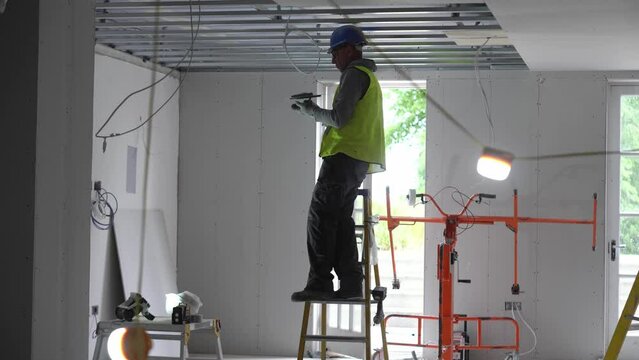 Hard male work on construction site. Two professional workers in special uniforms Contractors Safety Hats repairing ceiling wall inside building. Builders' equipment at workplace. industrial premises