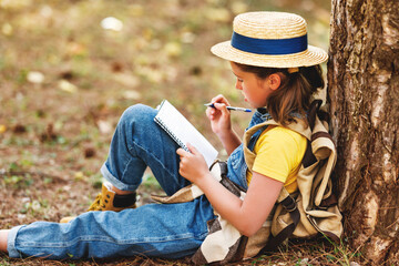 child girl  takes notes in a notebook while walking through   forest
