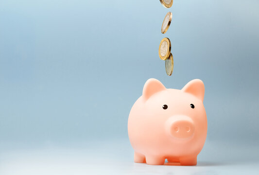 Pink piggy bank with falling coins on blue background