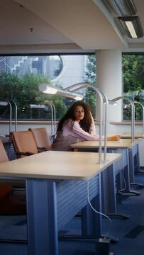 Young woman sitting at a work desk in an empty classroom, vertical