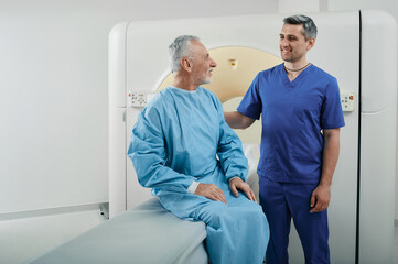 Radiographer talking with male patient in hospital radiology department prior to CT scan being...