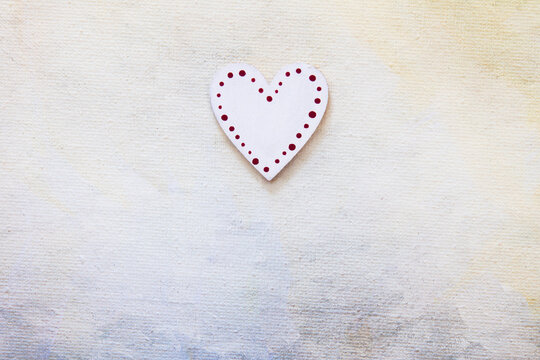 Single white heart with red dot outline on a painted canvas; Top down view of small heart with empty background